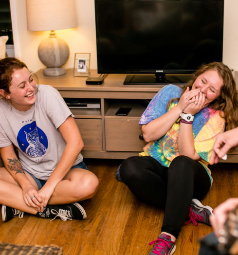 Two laughing housing students sitting on the floor.