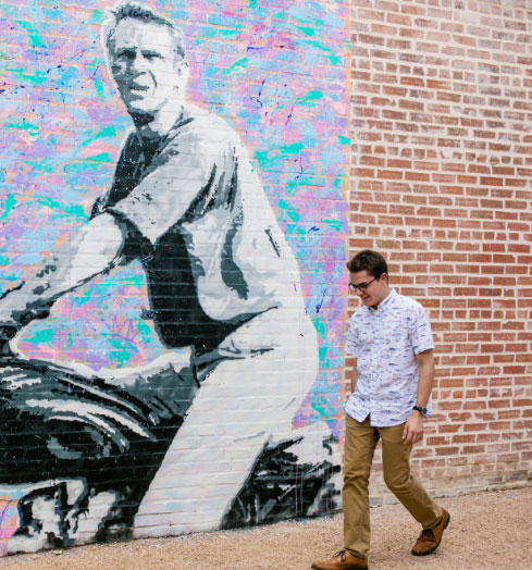 A student in Deep Ellum walking in front of a mural painted on a brick wall.