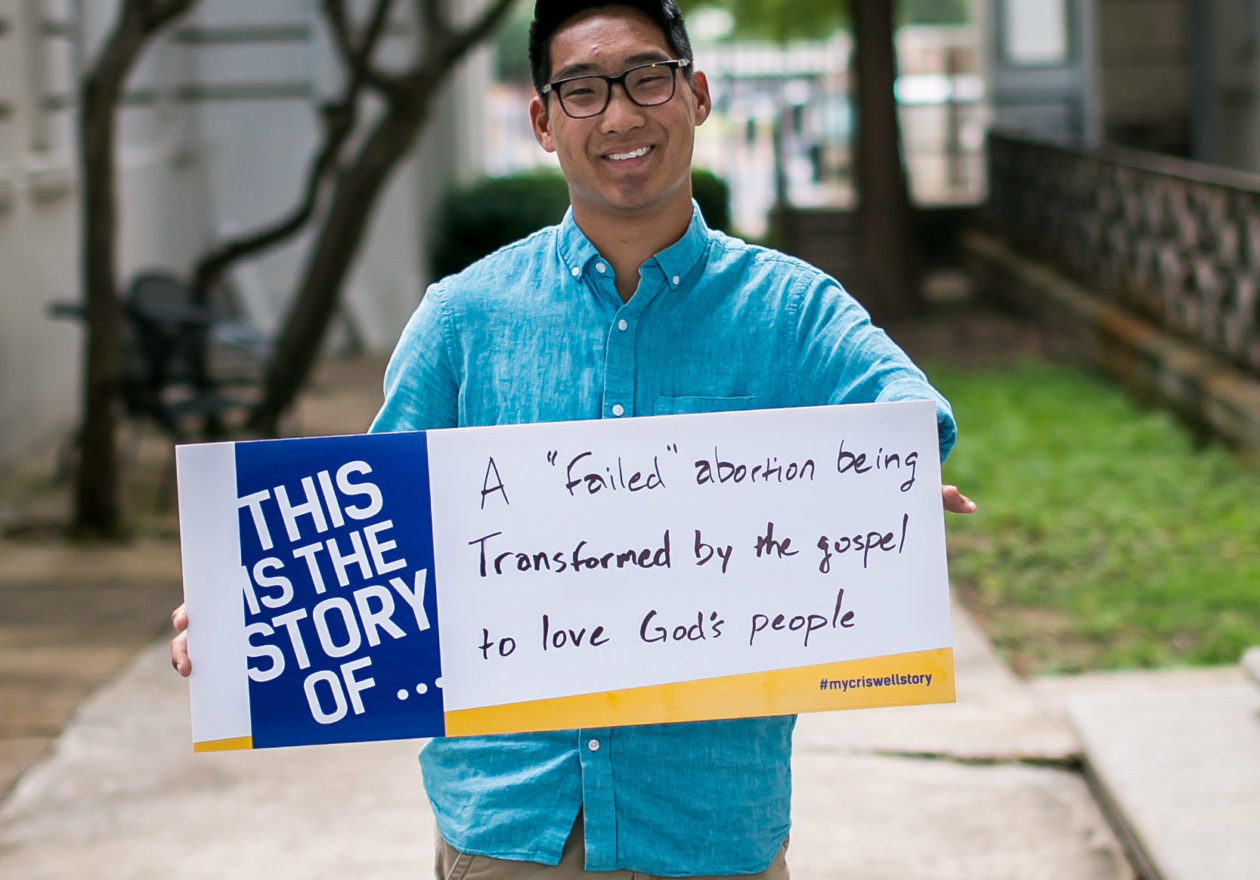 An undergraduate student holding signage that reads, "This is the story of a "failed" abortion being transformed by the gospel to love God's people."