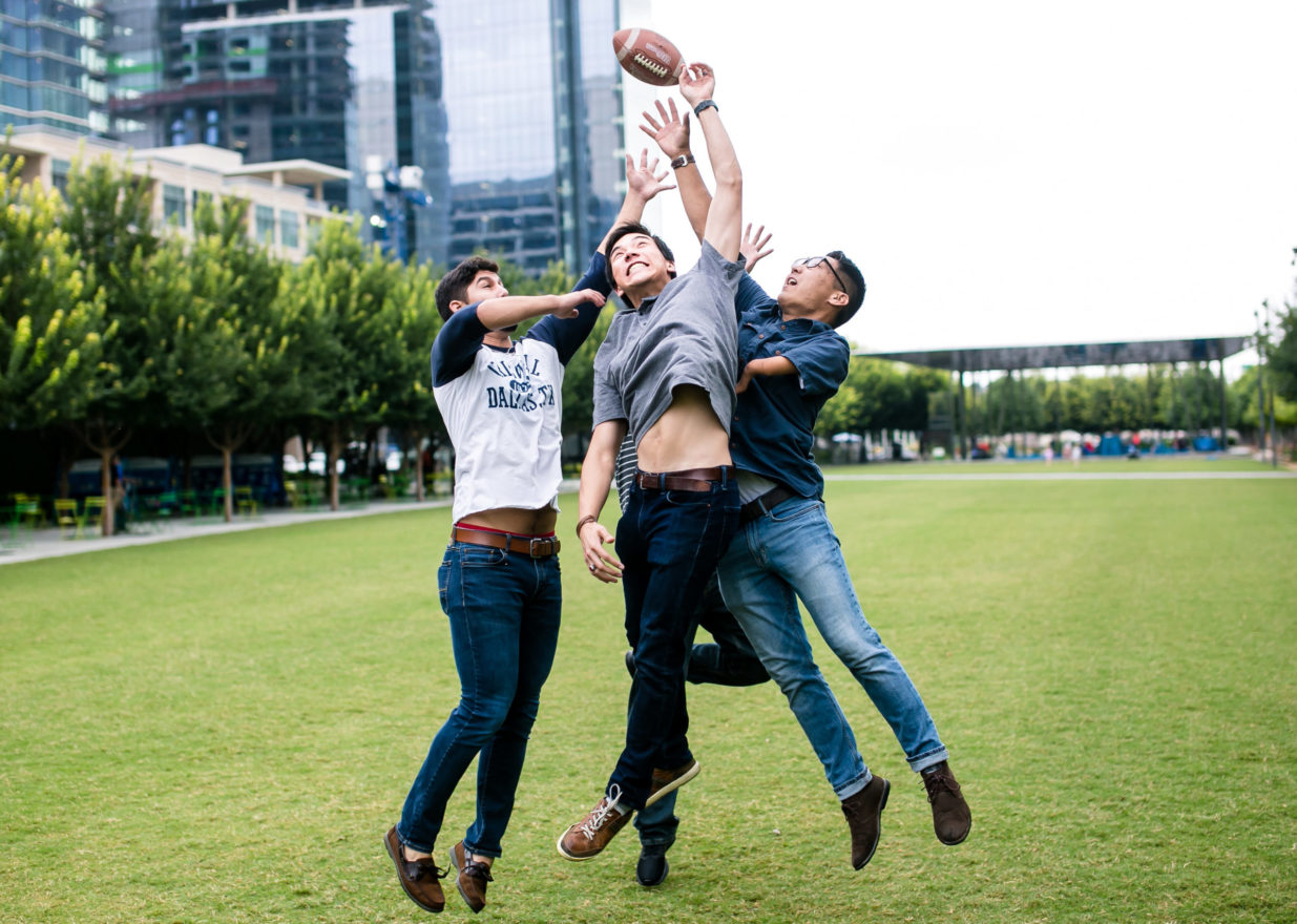 Four students vying to catch a football in an open green space.