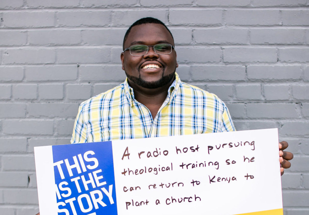 A smiling graduate student holding a sign that reads, "This is the story of a radio host pursuing theological training so he can return to Kenya to plant a church."