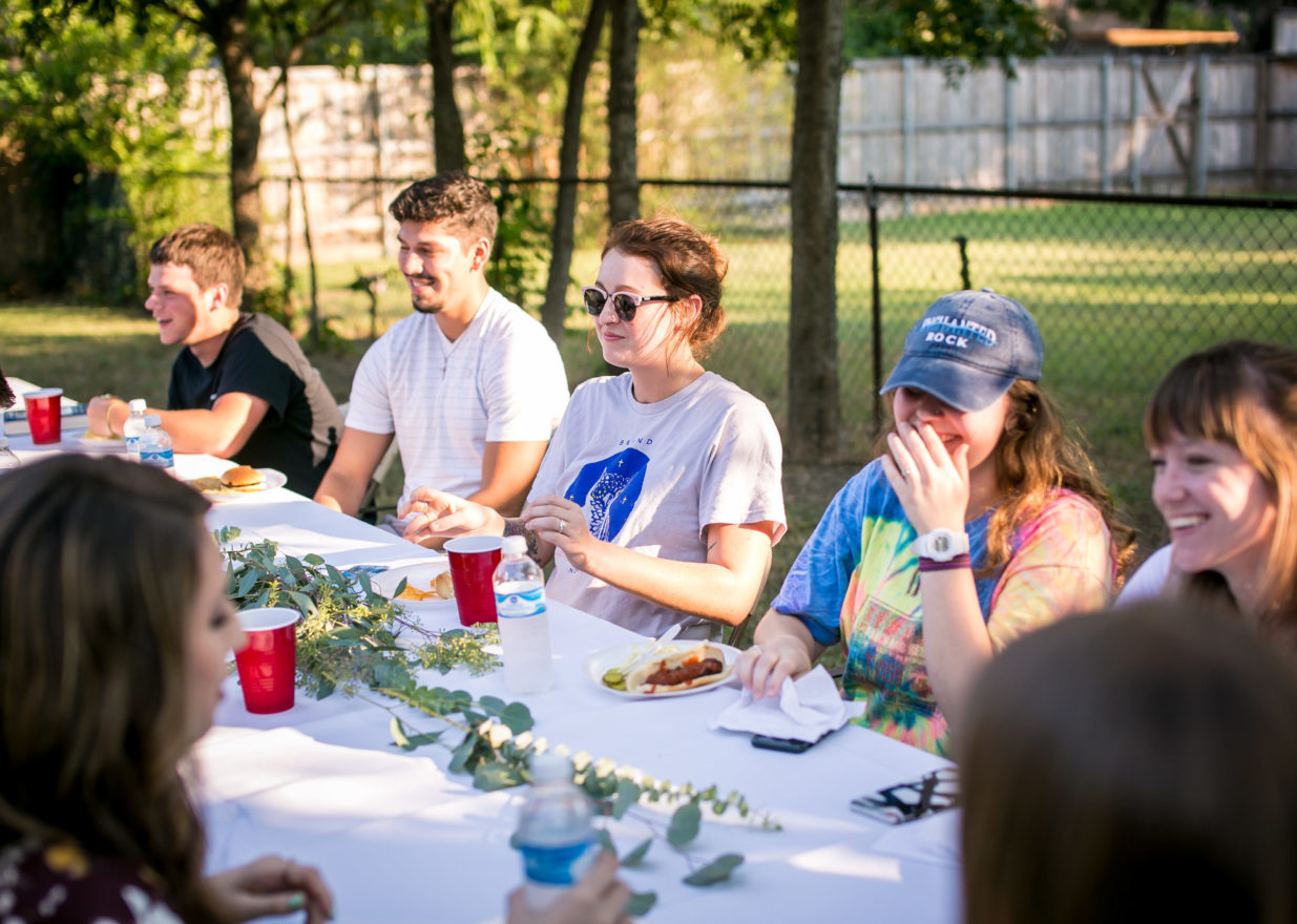 Students enjoying one another around the dinner table at a backyard barbecue.