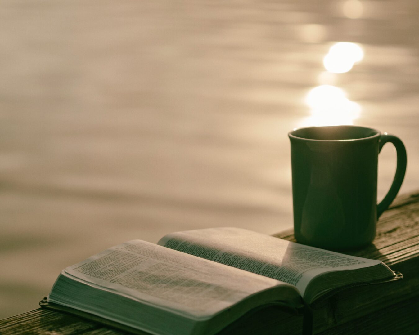 Bible open, coffee cup, lake in background